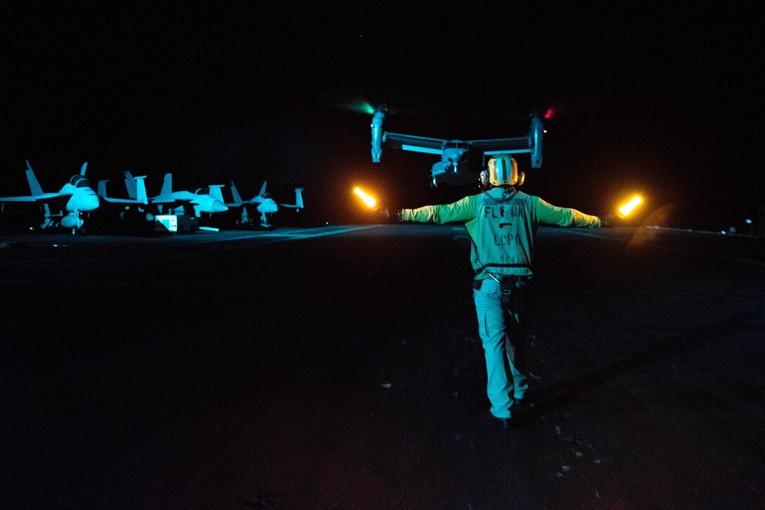 A sailor signals to an aircraft on a runway.