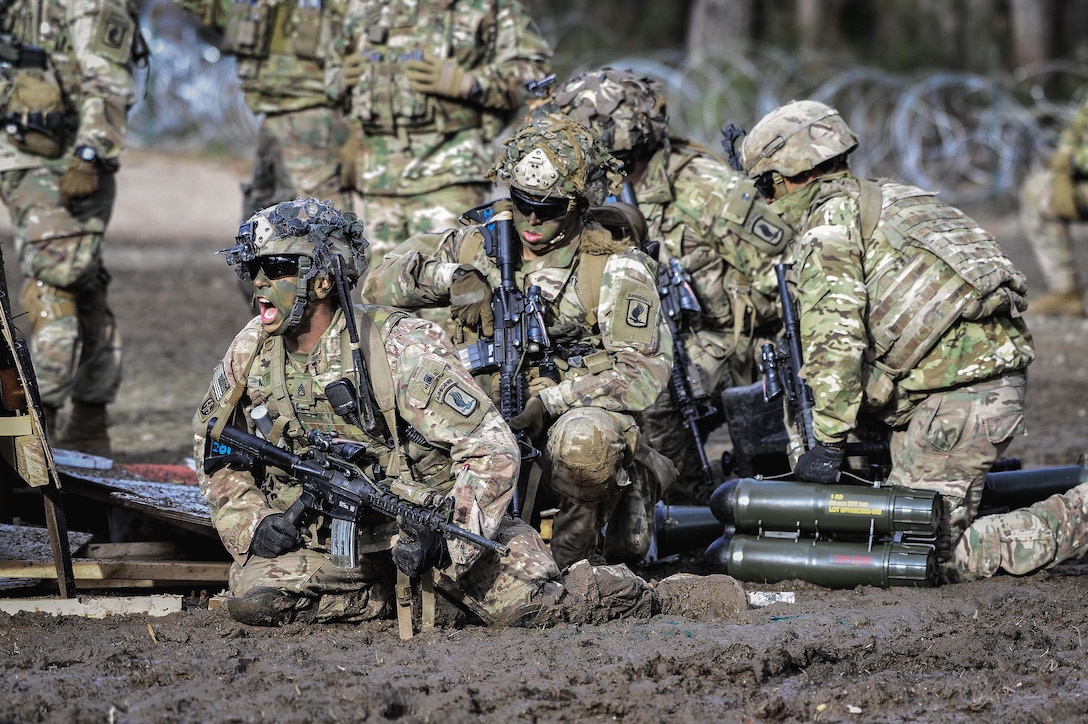 A soldier kneeling in dirt shouts as others crowd behind him.