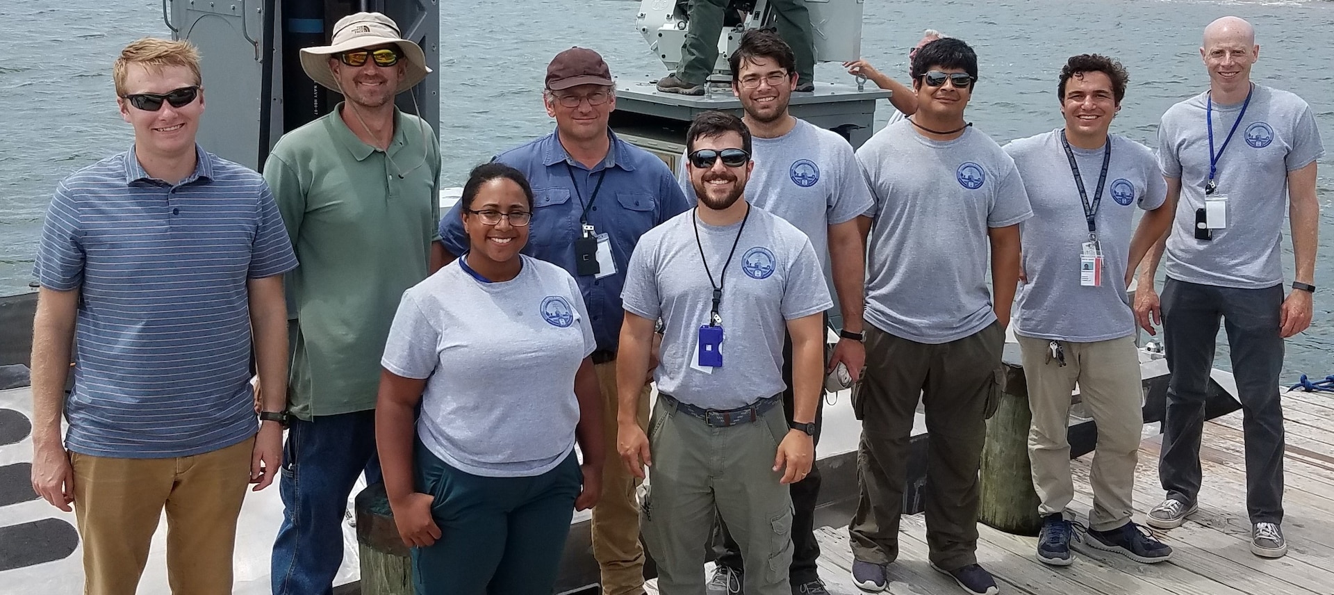 IMAGE: CAMP LEJEUNE, N.C. (July 19, 2019) — The Naval Surface Warfare Center Dahlgren Division (NSWCDD) Expeditionary Warfare Unmanned Surface Vessel (USV) team - pictured at the 2019 Advanced Naval Technology Exercise (ANTX) - demonstrated the Expeditionary Warfare USV’s ability to control inshore and littoral areas while identifying and engaging remote targets at the exercise. The 40-foot self-driving boat is integrated with a HellFire Longbow missile system and a .50 gun mounted on a remote weapon station along with radar, video, and infrared systems. ANTX 2019 is an event where academic, industry and Navy participants test new and emerging technologies. NSWCDD scientists and engineers standing left to right are: Colin Pritchard, Adam Broad, Logan Camacho, Robert Gripshover, Kevin Green, Michael Teresi, Mark Manzano, Joseph ‘Tripp’ Cannella, and Michael Liska.  (U.S. Navy photo/Released)