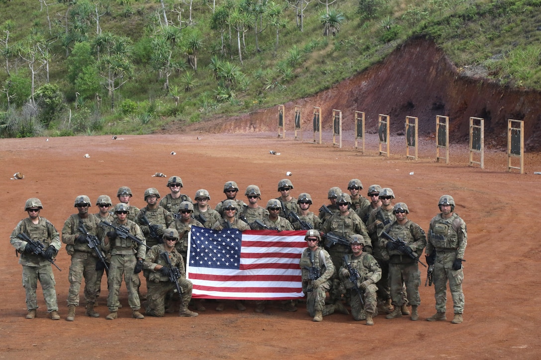 Soldiers pose for a photo on a range holding a U.S. flag.