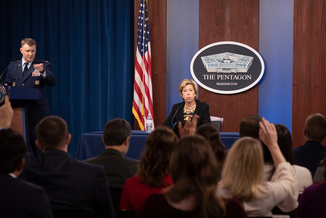 Reporters raise their hands as a service member and civilian