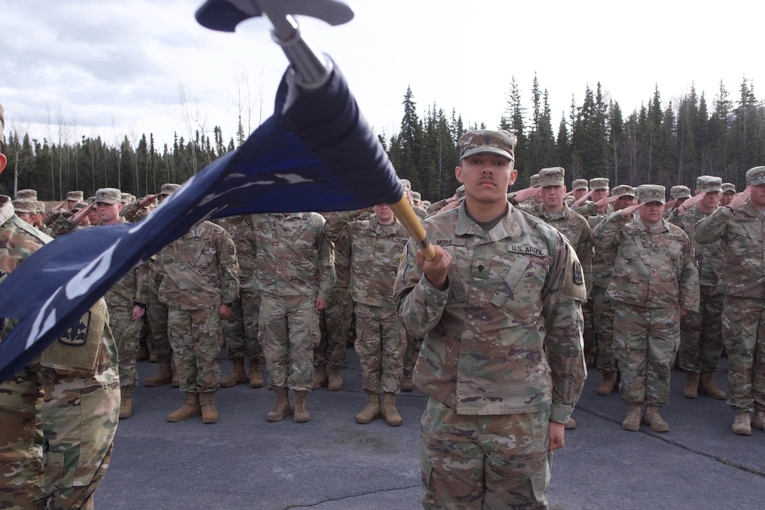 A soldier standing in front of a formation holds a flag.
