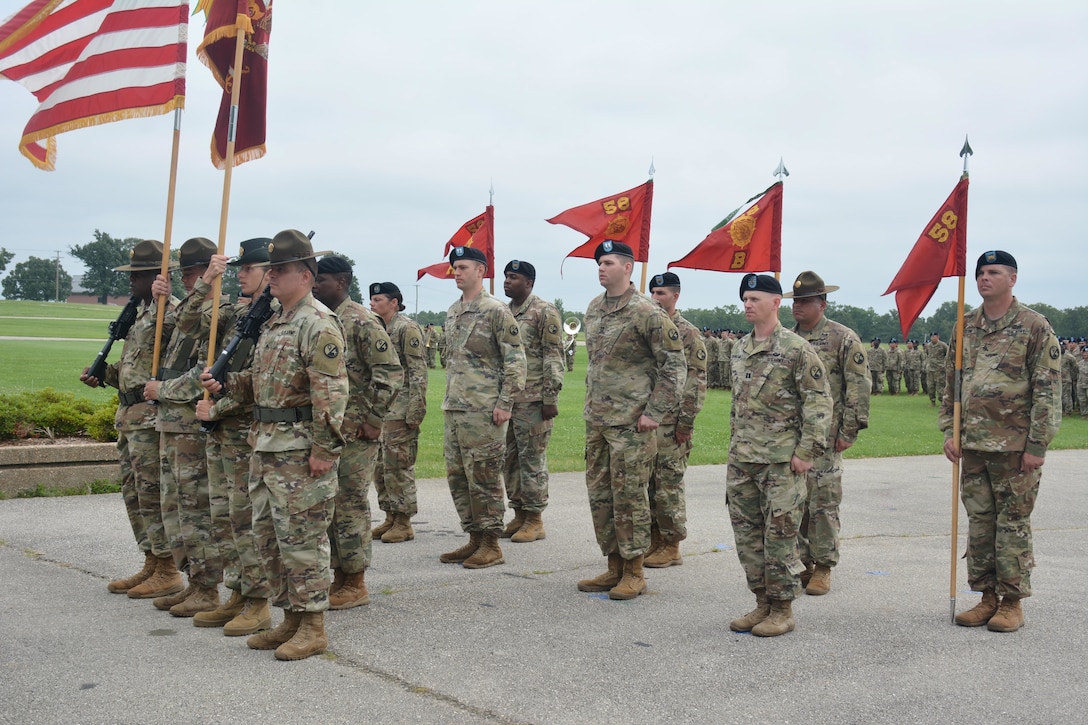 Soldiers, some holding flags, stand in formation on a paved area.