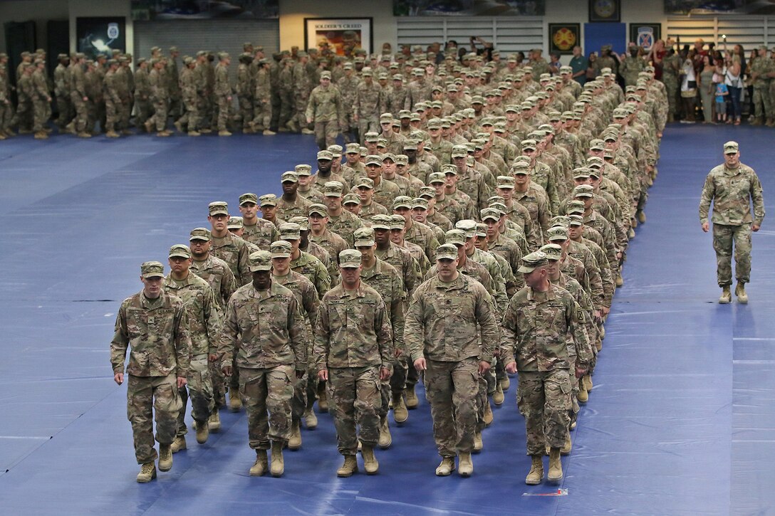 Soldiers stand in formation on a blue floor in a gym-type room.