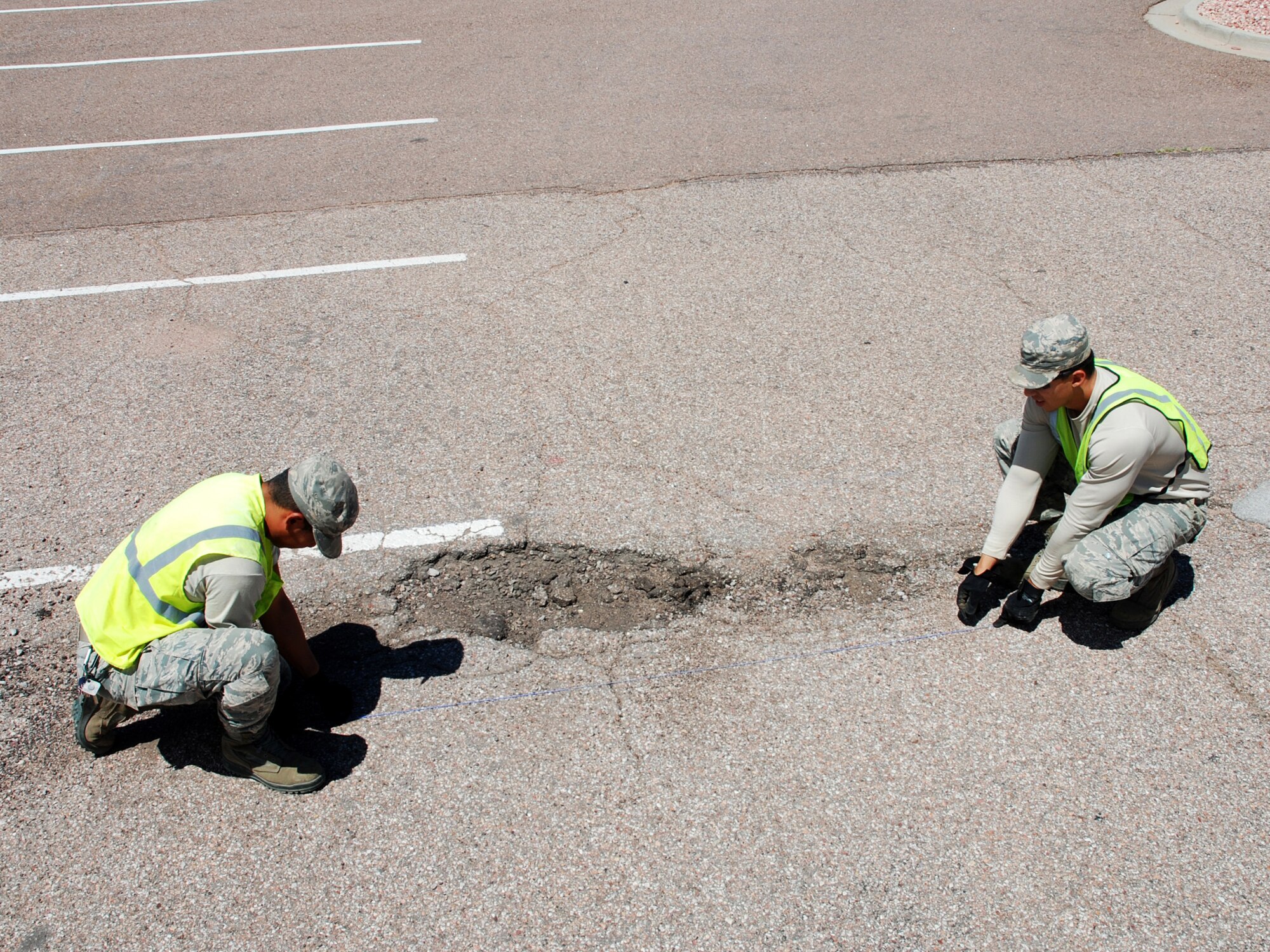 Water and major temperature fluctuations put heavy wear and tear on the roads at Peterson Air Force Base, Colorado. Dirt Boyz like Senior Airman Lemuel Travis, 21st Civil Engineer Squadron heavy equipment operator, left, and Senior Airman Daniel Acevedo-Chacon, 21st Civil Engineering Squadron heavy equipment operator, plan where to cut into the roadway as part of the process of repairing a pothole, Aug. 15, 2019. (U.S. Air Force Photo by Griffin Swartzell)