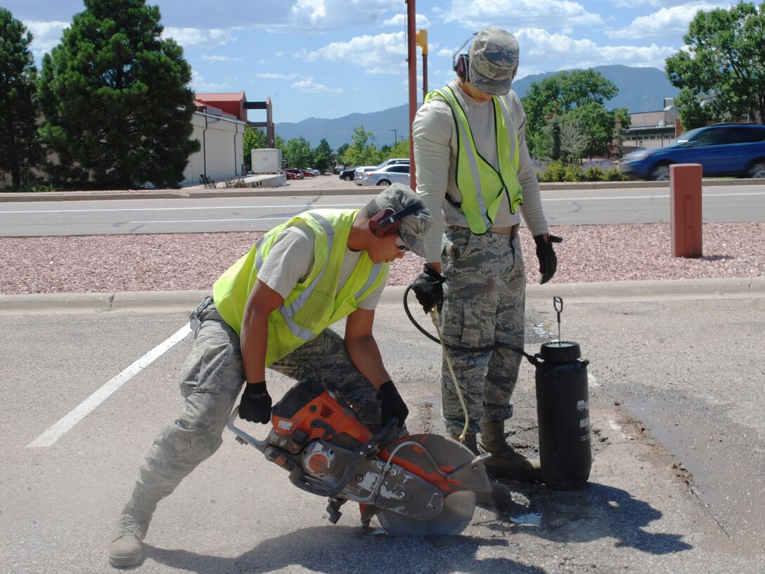 Senior Airman Lemuel Travis, 21st Civil Engineering Squadron heavy equipment operator, left, and Senior Airman Daniel Acevedo-Chacon, 21st Civil Engineering Squadron heavy equipment operator, start repairs on a pothole, Aug. 15, 2019. While Travis operates a concrete saw, Acevedo-Chacon sprays it with water to prevent overheating. It takes hard work and diligence to keep the roads clear and in good repair on Peterson Air Force Base, Colorado, but that’s what Dirt Boyz Travis and Acevedo-Chacon do. (U.S. Air Force Photo by Griffin Swartzell)