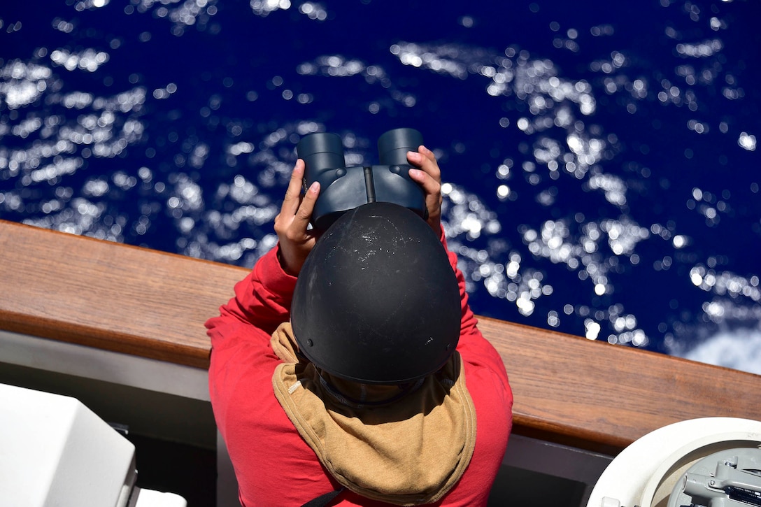 From above; a Coast Guardsman uses binoculars to look out at sea.