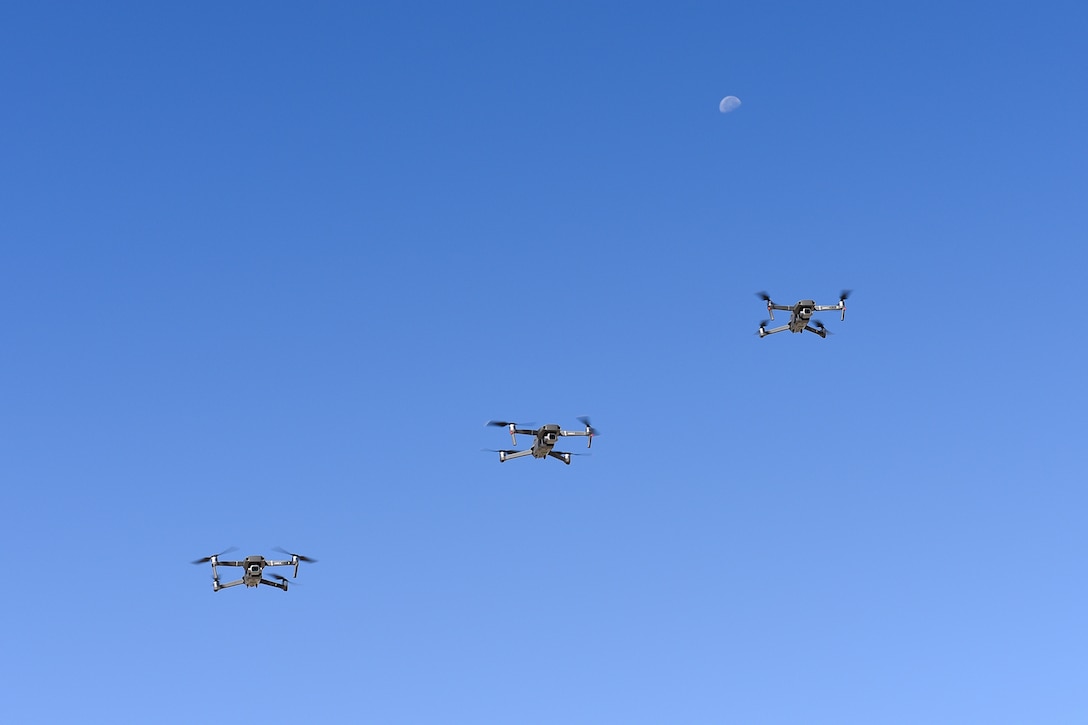 Three unmanned aerial systems fly in a row.