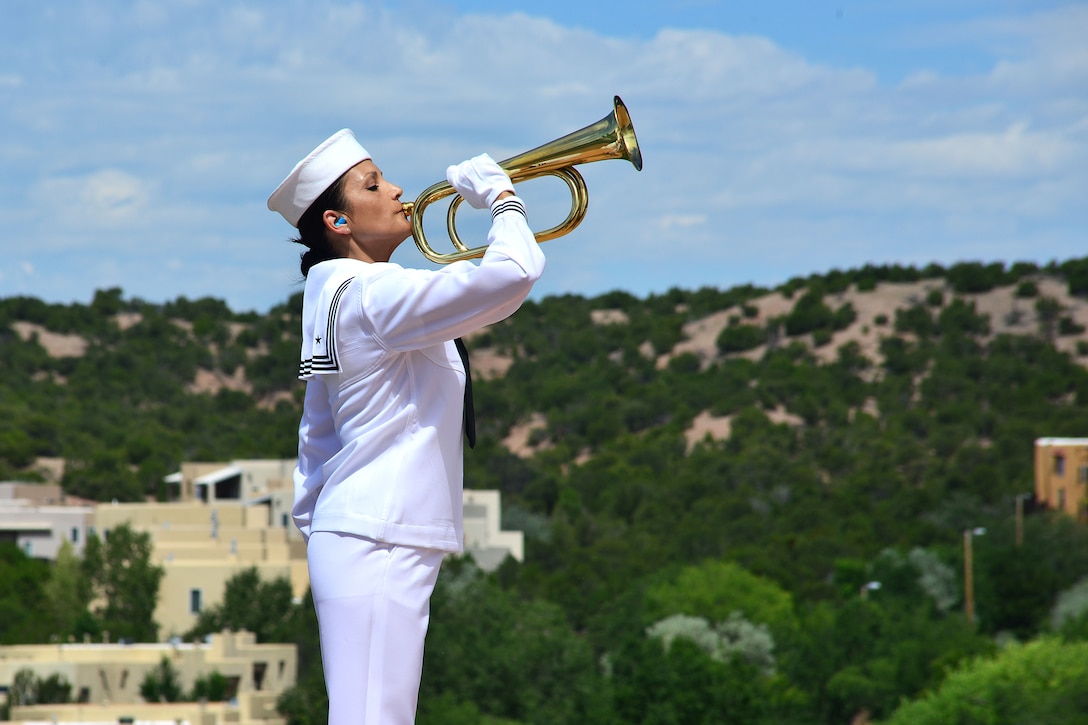A female sailor plays a trumpet at a military funeral.