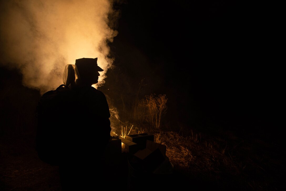 A Marine's head is silhouetted against a lit flare.
