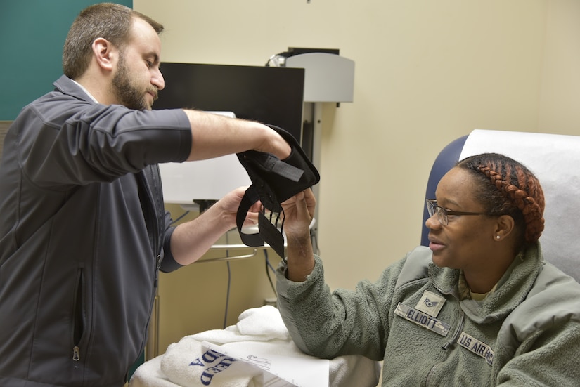 A man in a gray jacket puts a blood pressure cuff on a seated service member.