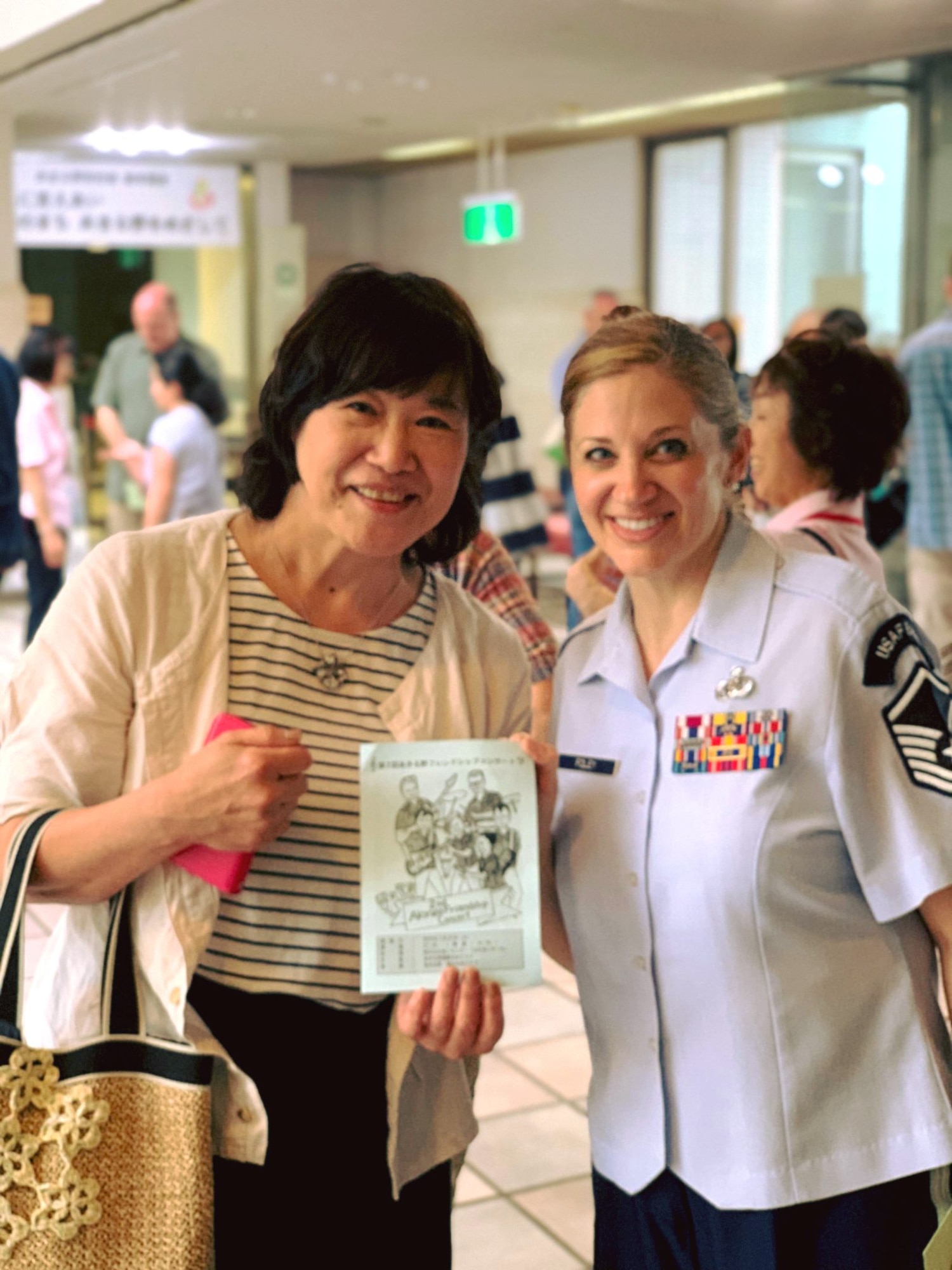 A U.S. Air Force Band of the Pacific Airman takes a photo with an artist who gave the band a piece of artwork after one of their performances. (Courtesy photo)
