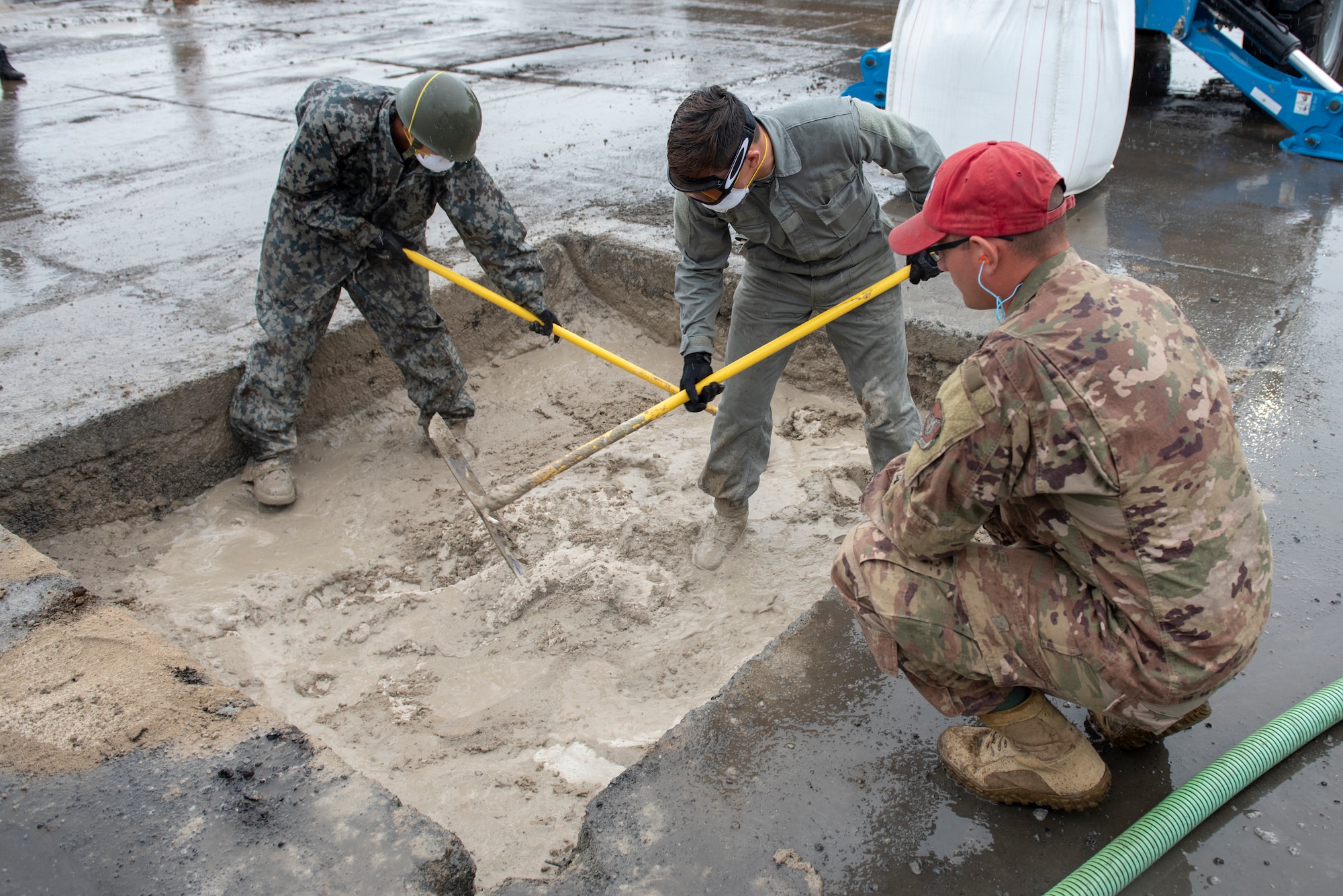 Training cadre from the 554th RED HORSE Squadron out of Andersen Air Force Base, Guam, oversees U.S. Air Force and Japan Air Self-Defense Force civil engineers mix water and flow able fill rapid set concrete to complete the backfill portion of rapid airfield damage repair during Pacific Unity 2019 at Yokota Air Base, Japan, August 23, 2019.