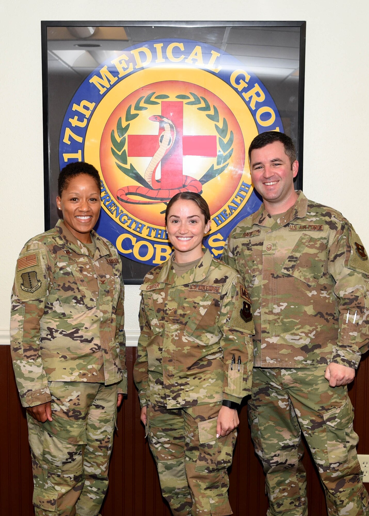 U.S. Air Force Airman 1st Class Breanna Carter, 17th Medical Group family practice medical technician, center, is recognized by Col. Lauren Byrd, 17th Medical Group commander, left, and Master Sgt. Steven Baer, 17th Medical Operations Squadron superintendent, right, as July’s Medic of the Month at the Ross Clinic on Goodfellow Air Force Base, Texas, August 19, 2019.  Carter has led multiple safety huddles and crafted schedules to maximize team efficiency for over 400 patients. (U.S. Air Force photo by Airman 1st Class Abbey Rieves/Released)