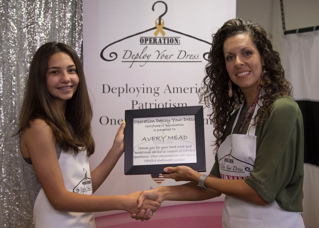 Avery Mead, age 14, daughter of U.S. Air Force Chief Master Sgt. Kevin Mead, 733rd Logistic Readiness Squadron superintendent receives an award from Kelly Day, Operation Deploy Your Dress volunteer, during the organization’s seasonal grand-opening at Joint Base Langley-Eustis, Virginia, Aug. 27, 2019.