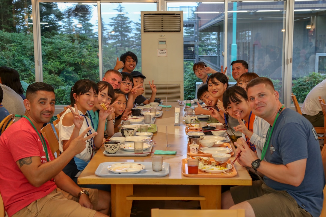 キャンプ富士の隊員と地域のボランティアと小学生が一緒に食事を食べ、カメラにポーズ。静岡県御殿場市にある国立中央青少年交流の家で地域の小学５・６年生を対象にしたイングリッシュ・キャンプが開催され、キャンプ富士の海兵隊員らが全面協力しました。