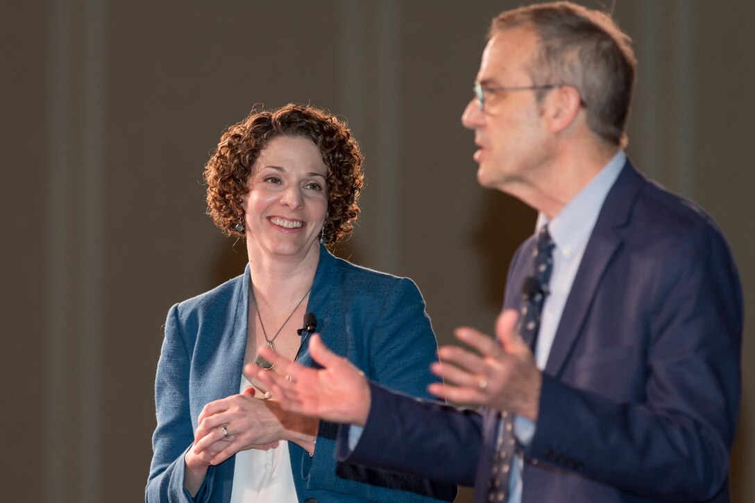 A woman looks on as a man speaks.