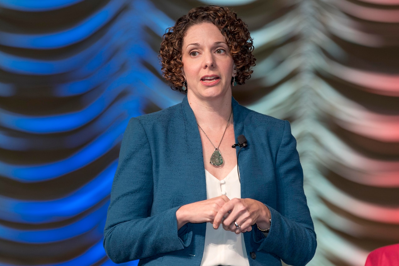 A woman gestures while speaking from a stage.