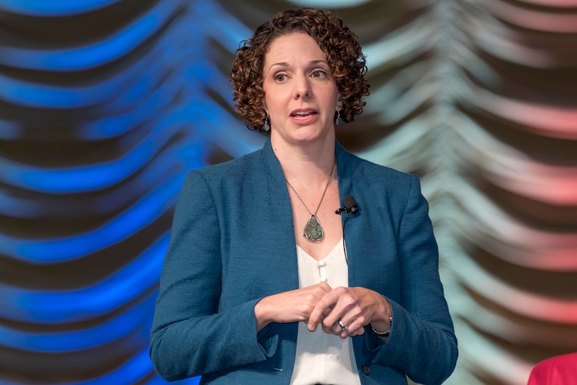 A woman gestures while speaking from a stage.