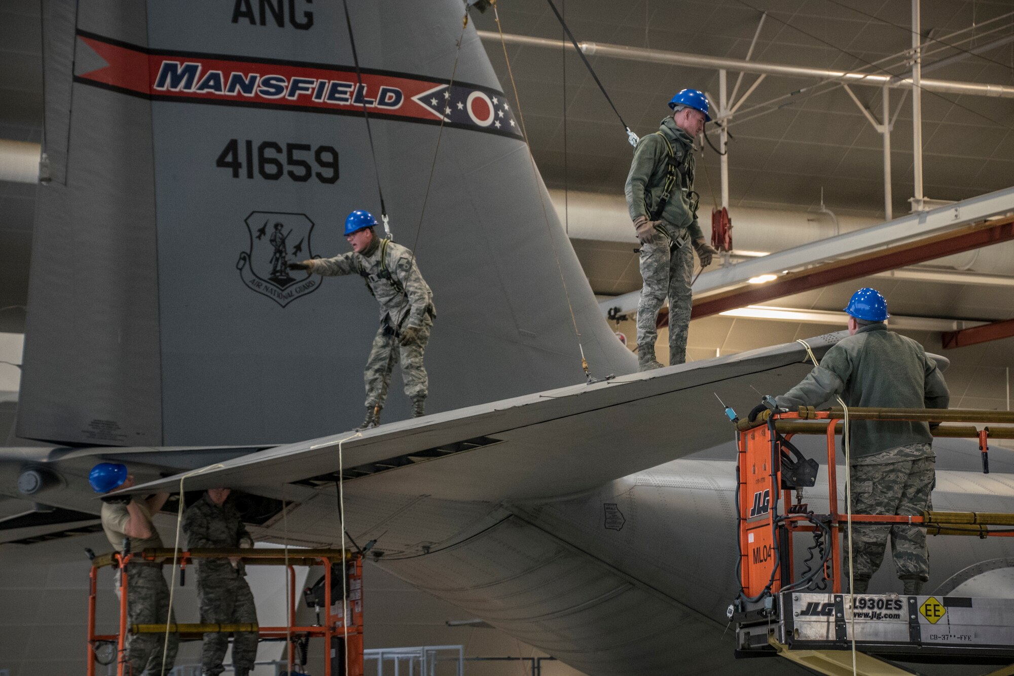 A photo of five military members walking on and around the tail of a C-130 aircraft while it was parked in the hanger.