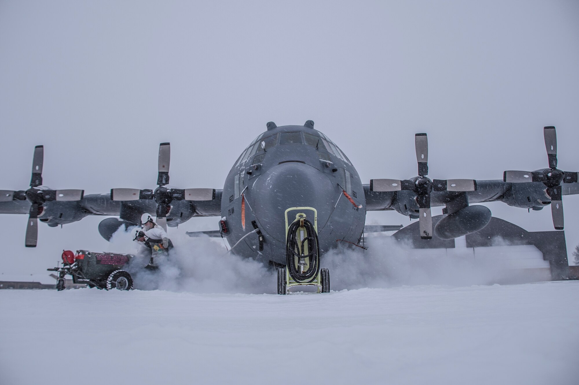 A photo of a C-130 on a snowy flight line surrounded by fog from refilling liquid oxygen.