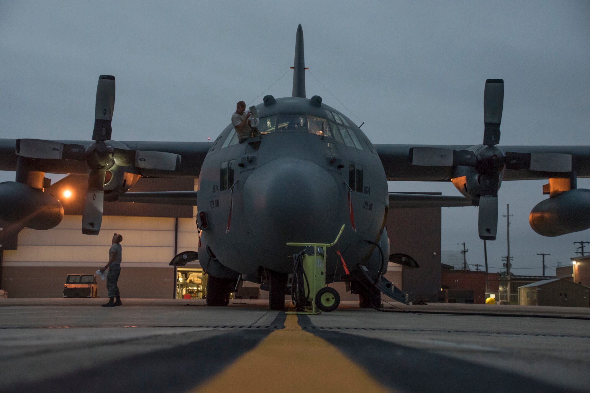 A photo of two military members working on a C-130 early morning on the flight line.