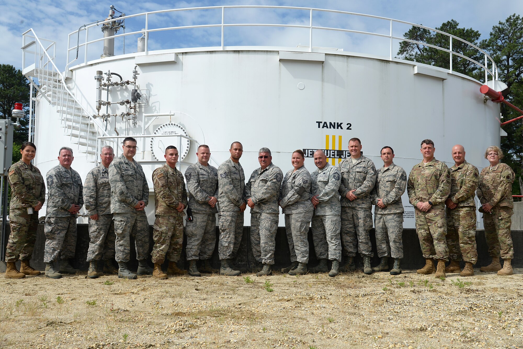 A picture of The 177th Fighter Wing Commander, Command Chief and various members of the Wing posing for a photograph in front of a jet fuel tank.