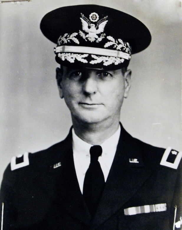 A soldier poses for a photo wearing his dress uniform and a decorated cap.