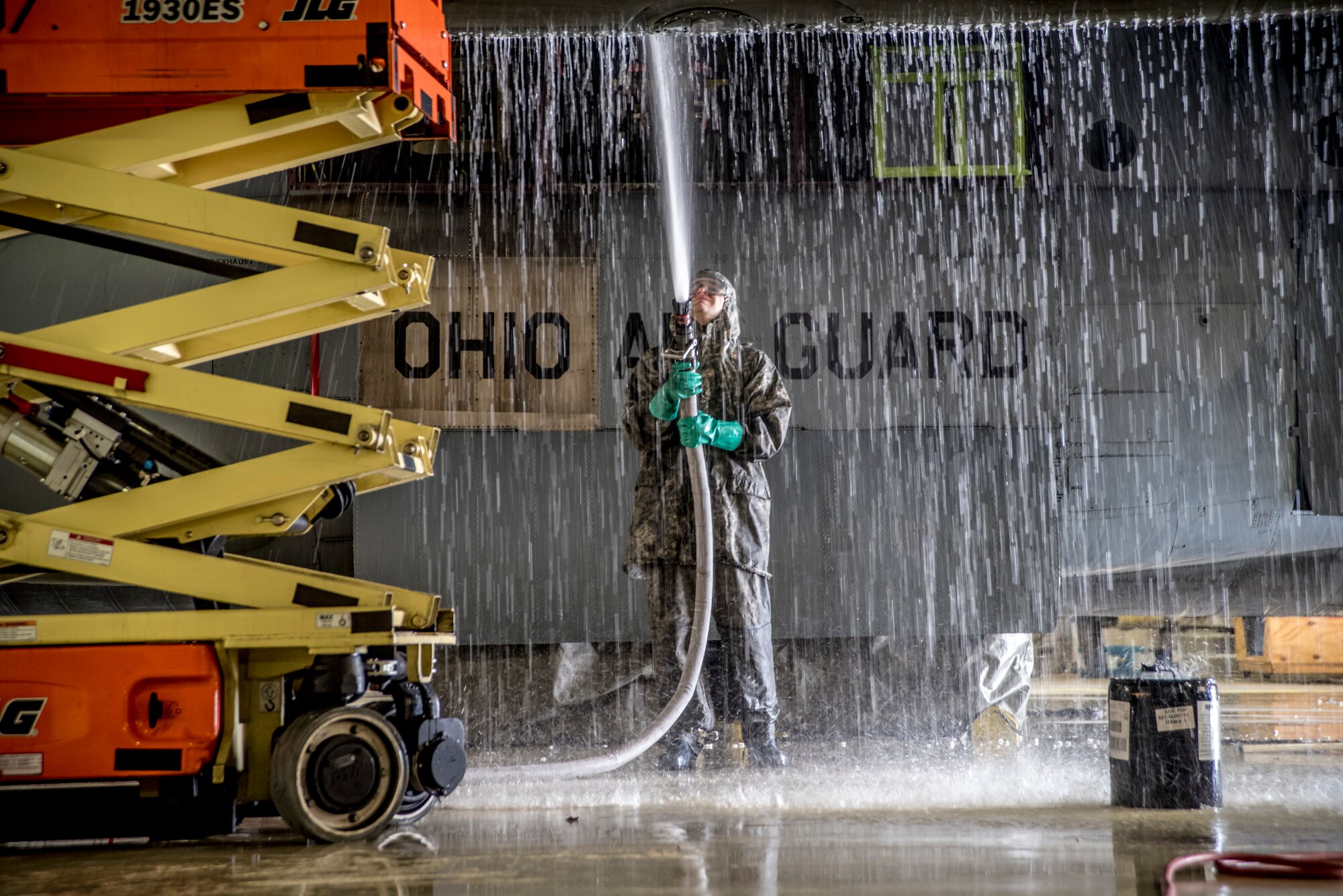 A photo of a military member using a hose to spray water onto a C-130 in the aircraft hanger.