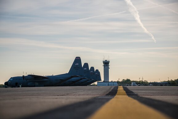 Photo of five C-130's on the flight line in front of the airport tower.