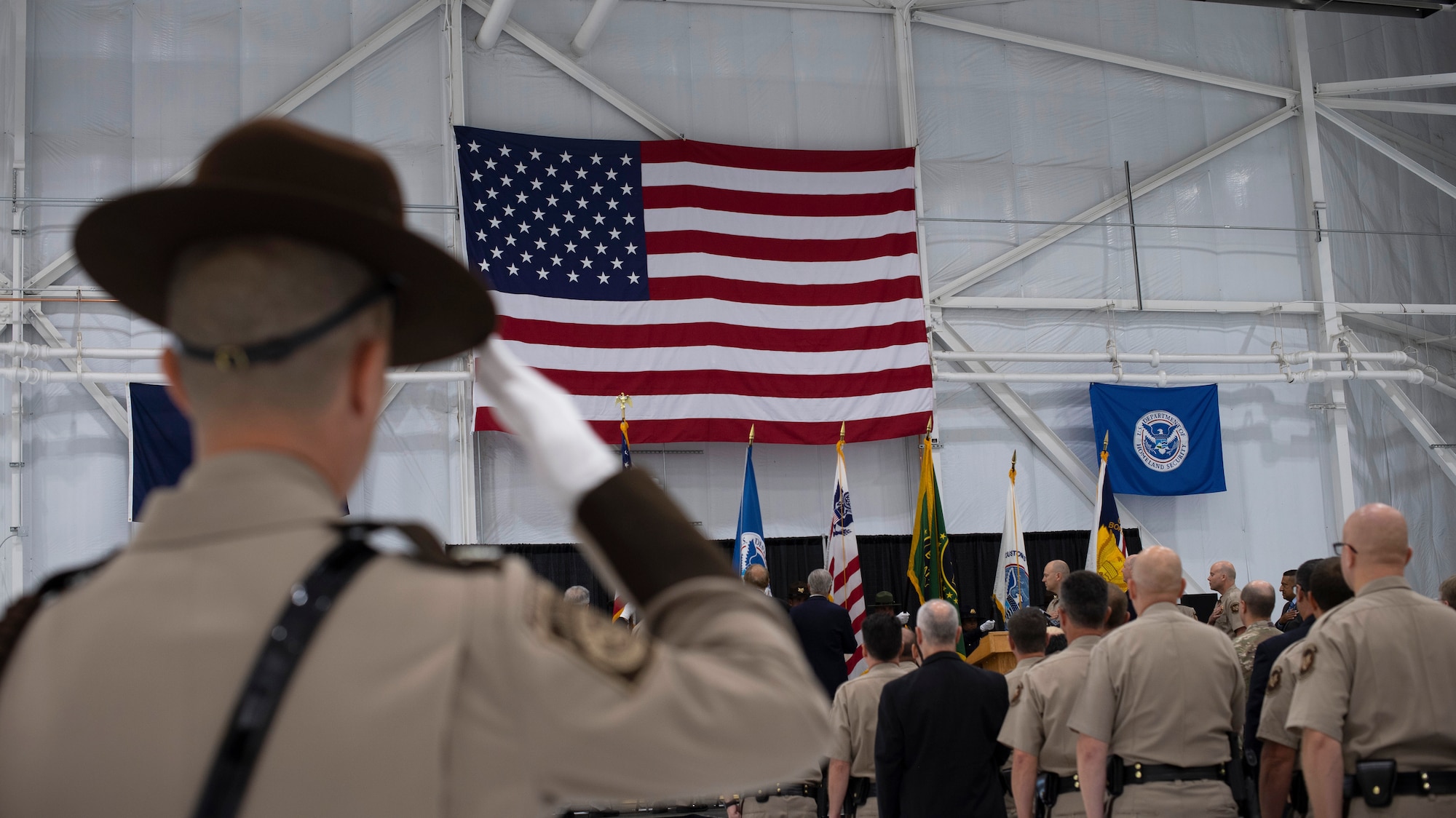 A U.S. Customs and Border Protection agent salutes the flag as the National Anthem is performed during a ceremony August 28, 2019, on Grand Forks Air Force Base, North Dakota. The ceremony was followed by a ribbon-cutting event to officiate the opening of a newly-renovated facility, which will house manned and unmanned CBP aircraft assigned to the National Air and Security Operations Center, Grand Forks. (U.S. Air Force photo by Senior Airman Elora J. Martinez)