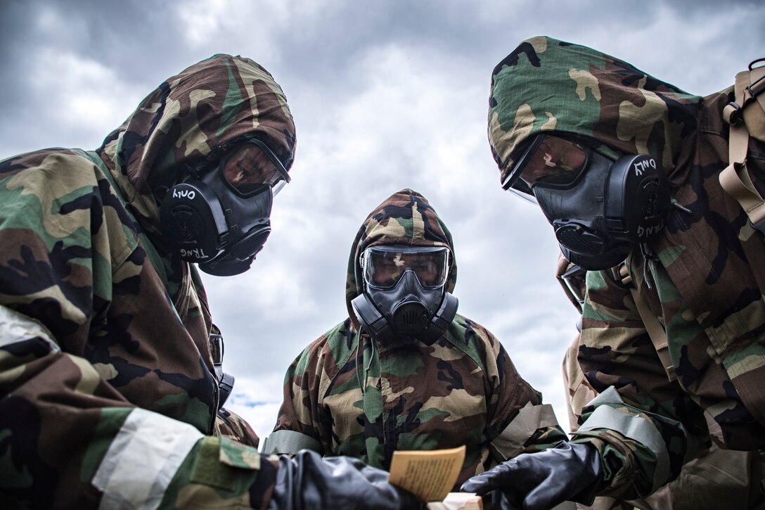 Photo of 3 military members in chemical gear, reviewing chemical papers.