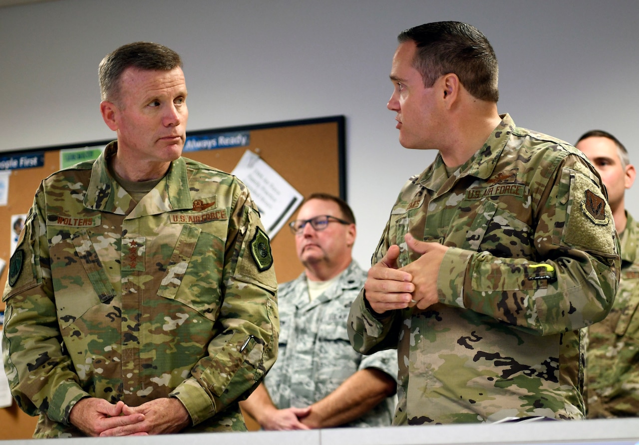 A man in military uniform is briefed by another service member.