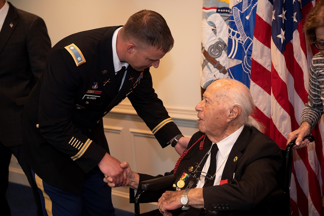 A man in a wheelchair is greeted by a man in a military uniform.