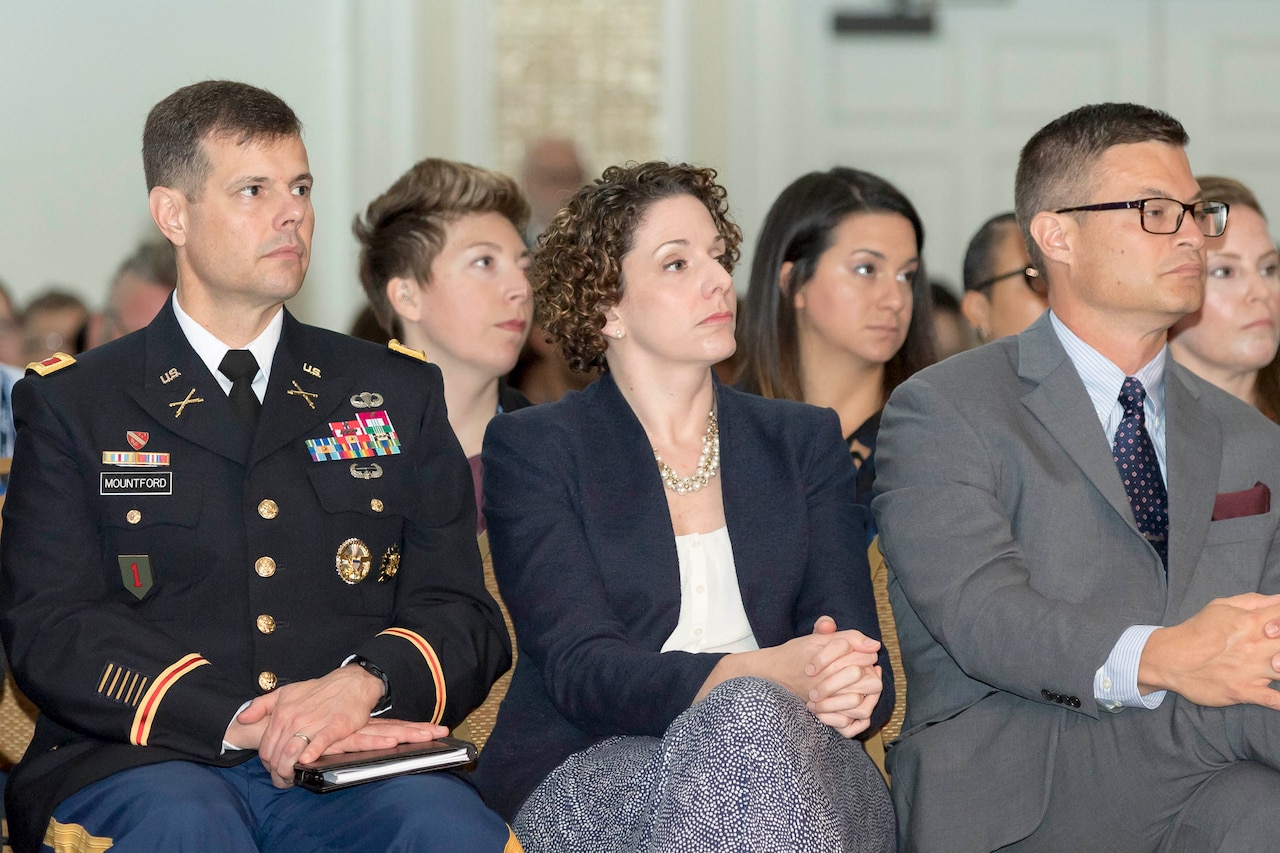 Three people sitting in chairs with others sitting behind.