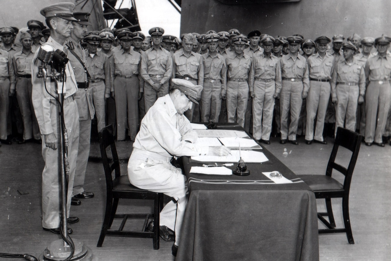 U.S. general signs document as other officers look on.