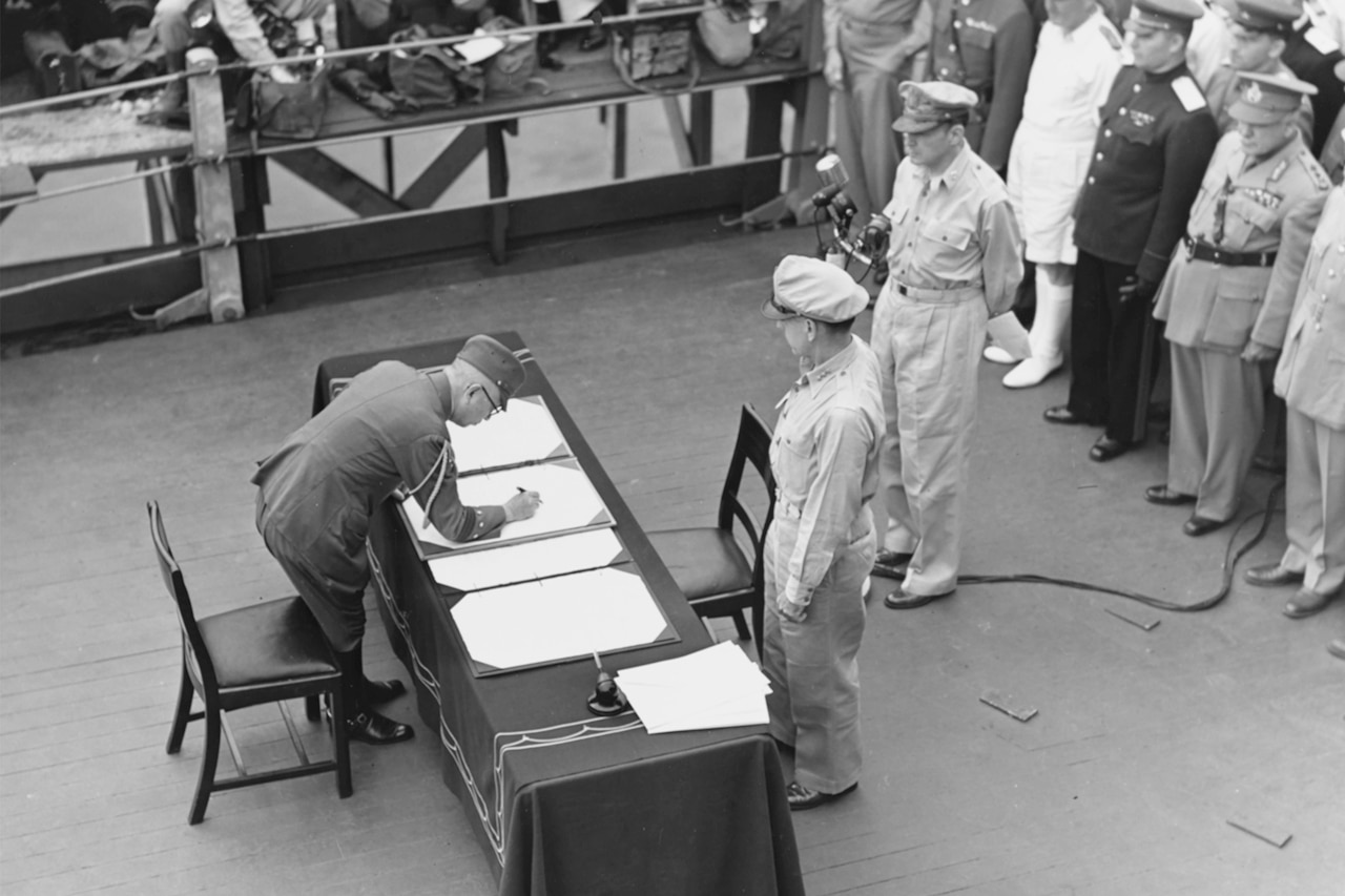 Japanese officer signs document.as Allied officers look on.