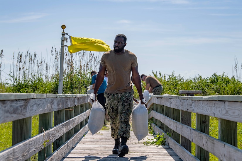 A sailor walks with sandbags.