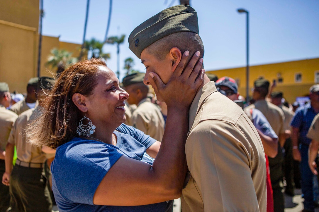 A woman holds a Marines face with her to hands in embrace.