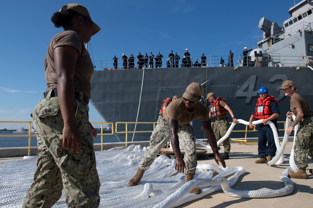 Sailors organize lines of rope on a ship.