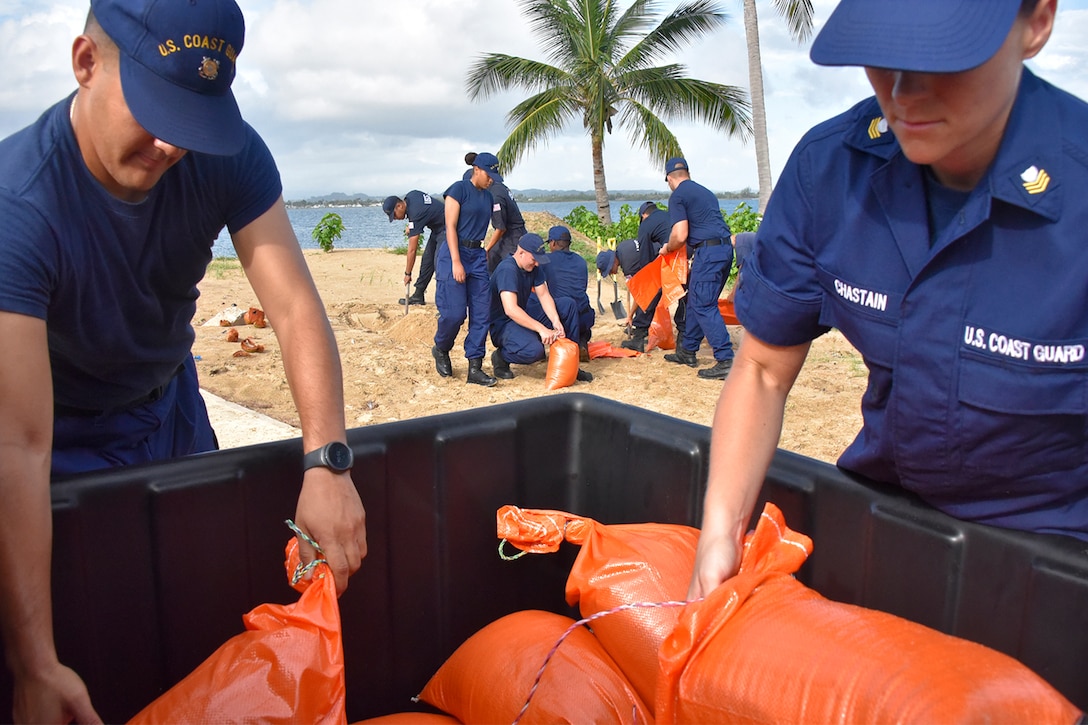 Coast Guard members place sandbags into a container.