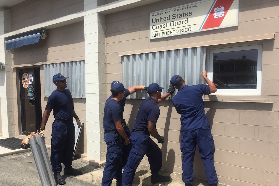 Coast Guard personnel attach hurricane shutters to windows.