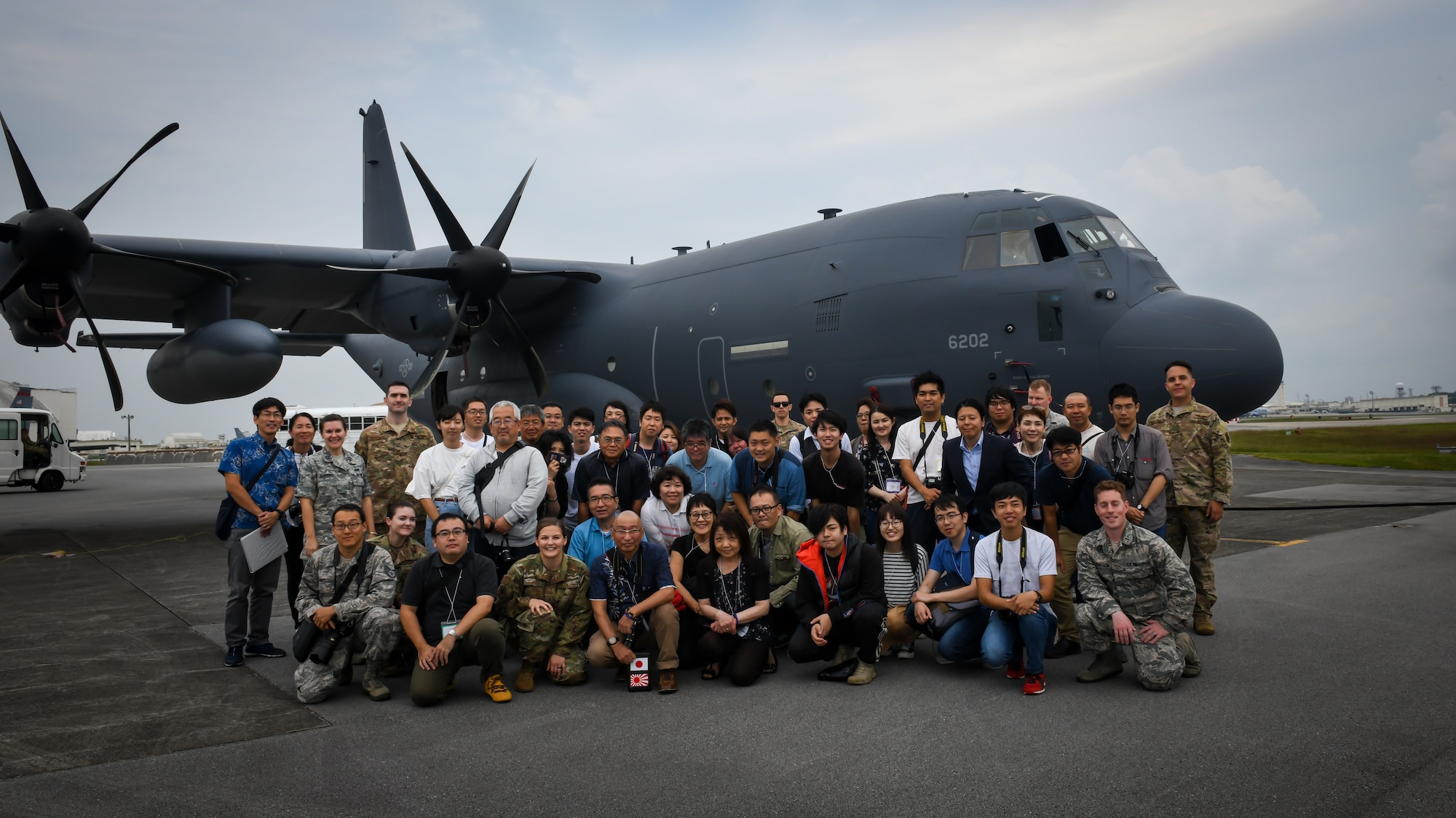2019年11月4日、第18航空団の空軍兵とツイッター・ツアーの参加者がMC-130JコマンドⅡの前で記念撮影。ツアーを通して、参加者は第18航空団の任務、憲兵中隊と沖縄県警の連携、嘉手納基地での環境管理と駐留する航空機について学んだ。（米国空軍・ベンジャミン・ロートン三等空曹撮影）