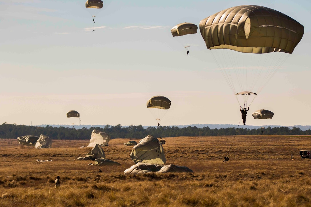 Soldiers wearing parachutes descend from the sky to the ground.