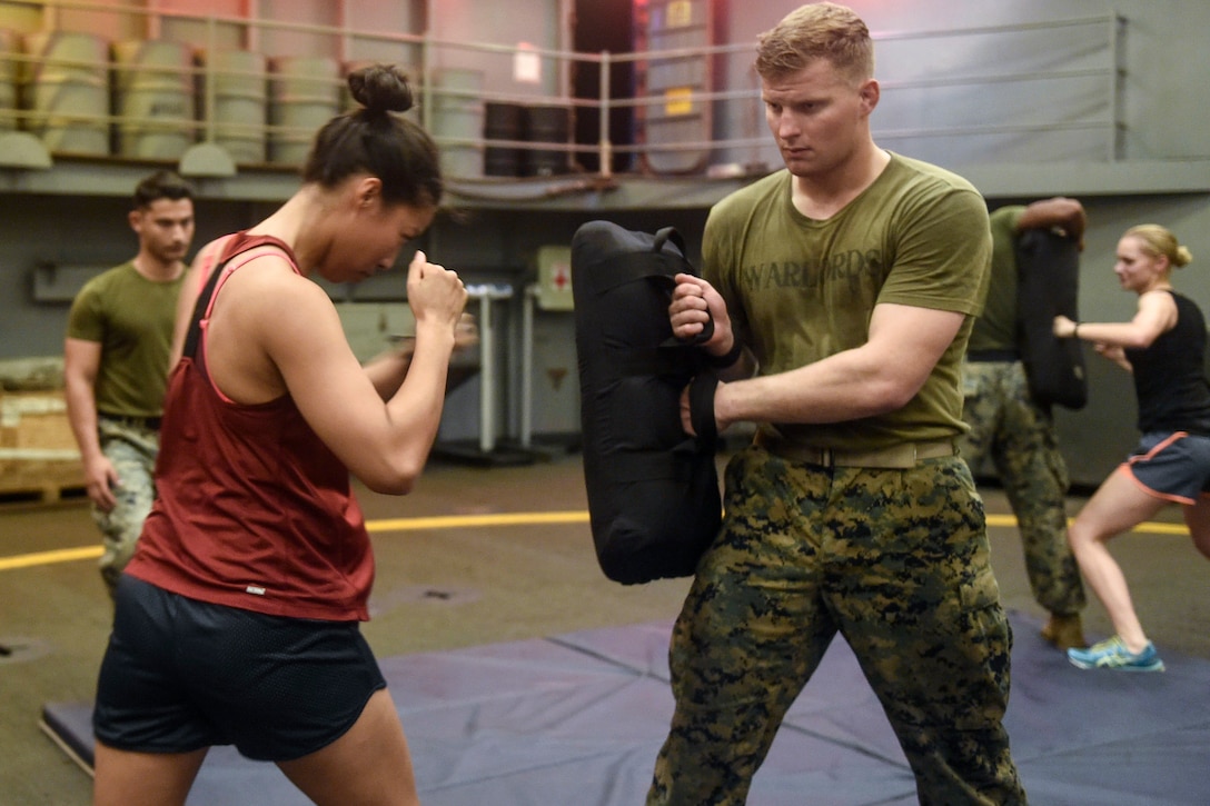 A sailor holds her fists up as a Marine holds a pad for her to punch.