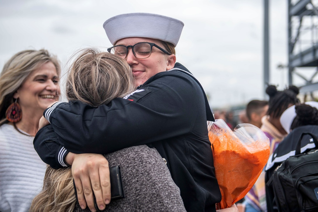 A sailor hugs another woman as a crowd mills about in the background.