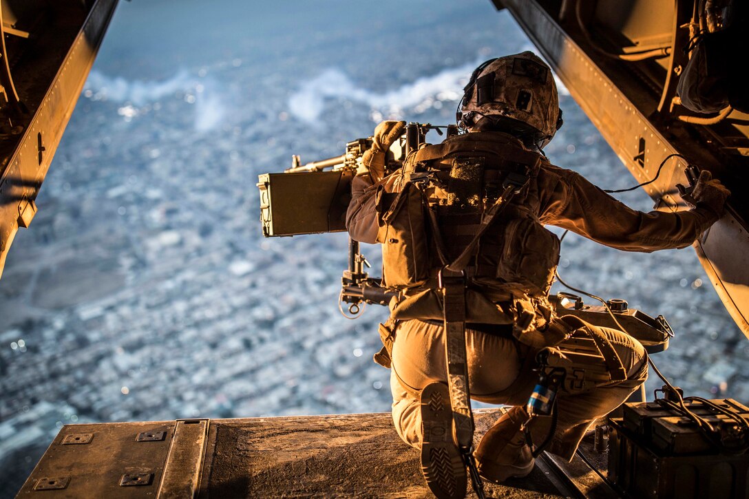 A Marine kneels at the back of an aircraft looking at the horizon.