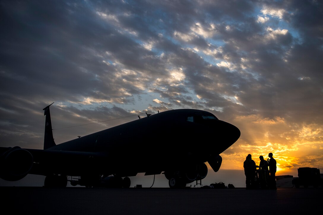 Airmen, shown in silhouette, stand on a flightline by a large aircraft.