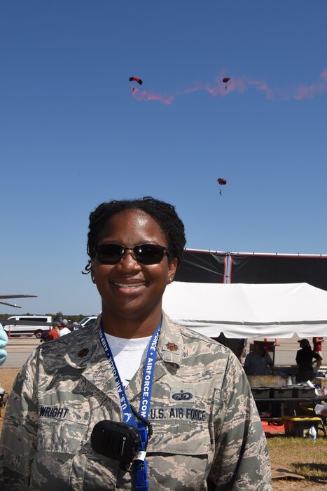 Photo shows Maj. LaToshia Wright, 2019 air show director, posing for a picture with the Army Black Daggers parachute jumpers performing in the background.