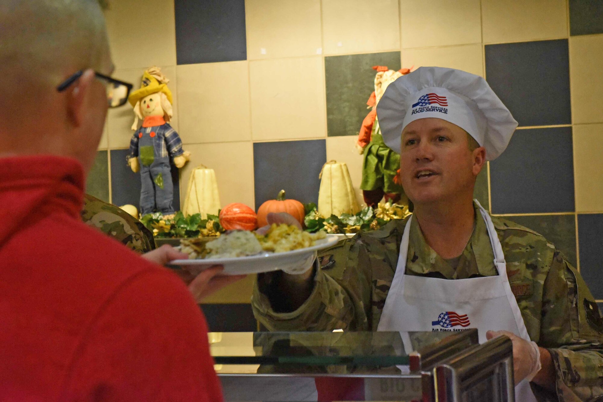 Airmen in chefs coat serve meals in cafeteria line
